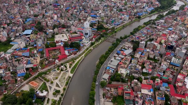 Aerial drone view of a walled river corridor cutting through the dense urban sprawl of a Nepalese city.