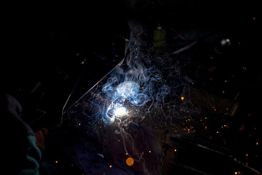 Welding old metal car part at workshop, sparks and smoke flying around, dark background, closeup detail