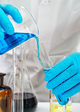 Hands in protective gloves pouring liquid from beaker to a smaller test tube, closeup detail. Chemical lab experiment or analysis