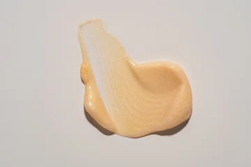 Gold shimmer body cream swatch texture on beige. Shiny nude liquid lotion smudge, glittering skincare moisturizer or gel highlighter sample © IKvyatkovskaya