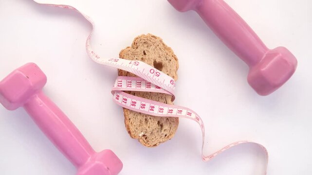 Dumbbells, slice of bread, and measuring tape implying diet and exercise concepts