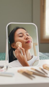 Vertical Screen : Young Asian girl beauty blogger looking at mirror makeup use makeup brush apply brush powder on cheek. Lifestyle people, Make up Natural look, Skin Care Cosmetics, Morning routine.