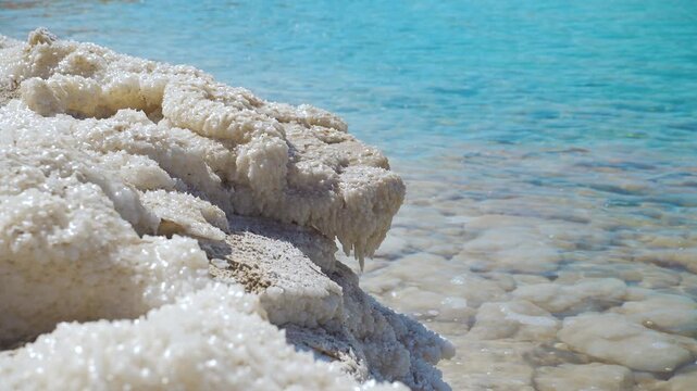 Dead Sea shore, sand and rocks completely covered with salt that looks like frozen ice crystals, calm clear water near