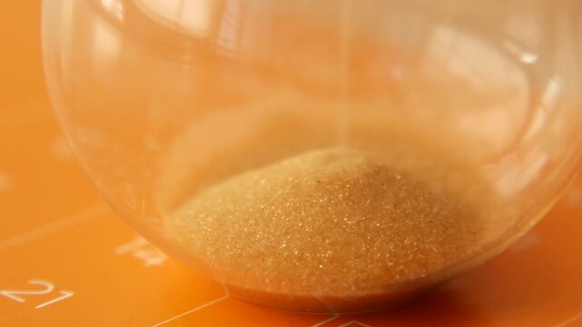 Macro view of hourglass with golden sand falling over orange desk calendar surface