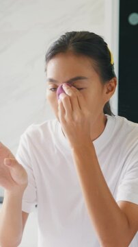 Vertical Screen : Young Asian happy woman looking at reflection in mirror use makeup sponge apply foundation on face in bathroom. Lifestyle and people, Natural Skin Care Cosmetics, Morning routine.