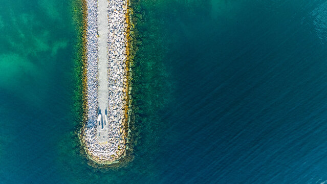 Top down aerial drone view of stone breakwater pier extending into deep blue ocean water with copy space
