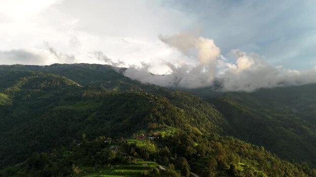 Aerial drone perspective of heavy storm clouds rolling over a dark, dramatic green mountain ridge in Nepal