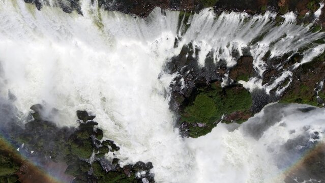 Top-down bird's-eye aerial view of churning waterfalls with a rainbow arc in the mist