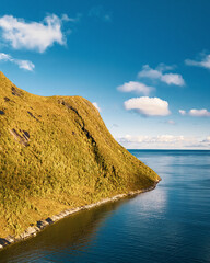 High angle vertical view of sunny mountain coast extending into blue ocean under bright sky with clouds in scandinavia with copy space © Quality by Simon