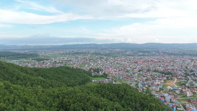 Wide panoramic drone shot of a massive sprawling metropolitan basin nestled in a valley surrounded by green forested hills under a cloudy sky.