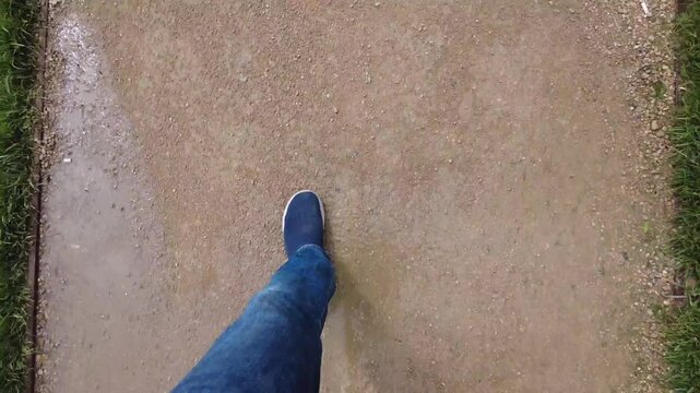 Low angle view of person walking on gravel path wearing blue jeans and sneakers