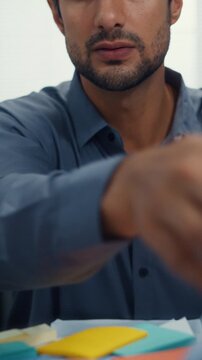 Closeup overworked young Latin businessman reading document in large stack of paperwork file at office desk. Tax audit deadline, accounting stress, corporate burnout, bookkeeping, bureaucracy concept.