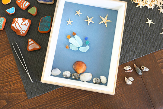 Upcycled sea glass shadow box beach decor craft. Eco friendly sustainable home decor styling. Creative summer hobby DIY workshop backdrop.