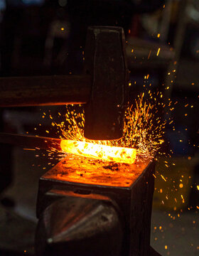 Heavy hammer striking red-hot glowing metal on an anvil, bright sparks exploding through dark forge workshop, dramatic firelight, industrial craftsmanship. Close-up.