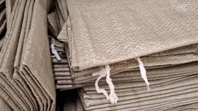 close-up of a large stack of woven plastic polypropylene bags tied with white strings, industrial heavy-duty packaging material and wholesale storage supply concept.