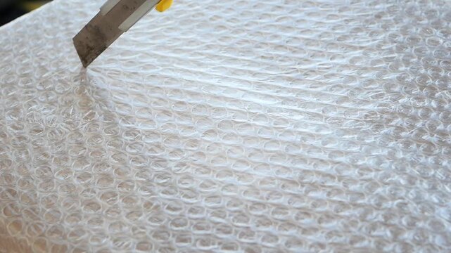 Person cutting bubble wrap with utility knife tool to open fragile package
