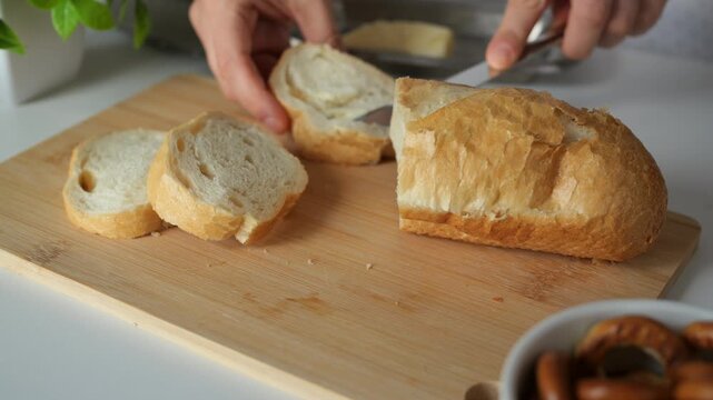 Spreading creamy butter onto bread slice shows simple home cooking preparation. Chef gently spreads soft dairy spread across freshly cut baguette loaf on wooden board for breakfast meal.