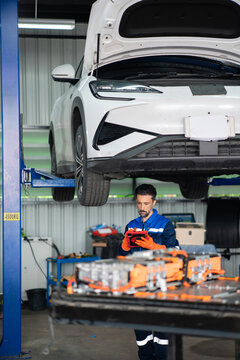 Battery inspection lets an electric vehicle mechanic check an open high voltage battery beneath a raised car using a tablet.
