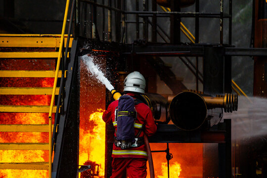 Firefighter spraying chemical foam hose to extinguish industrial plant fire