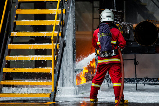 Firefighter spraying chemical foam hose to extinguish industrial plant fire