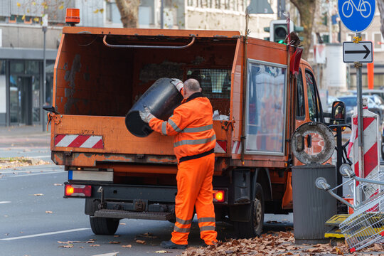 Municipal sanitation worker loads a waste bin into an orange garbage collection truck