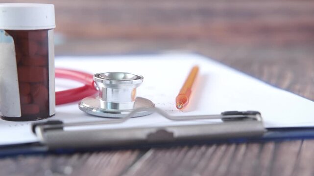 Healthcare supplies including stethoscope and medication bottles on wooden table with clipboard footage