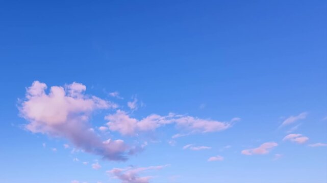 Sky transforms in a mesmerizing timelapse featuring soft pink, white, and light gray clouds drifting across a vibrant blue backdrop.