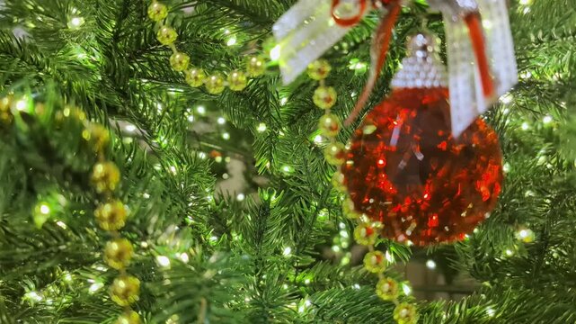 Green fir branches adorned with sparkling yellow bead garlands and bright decorative lights. Shiny red baubles with intricate patterns and festive bows enhance the holiday spirit of the Christmas.