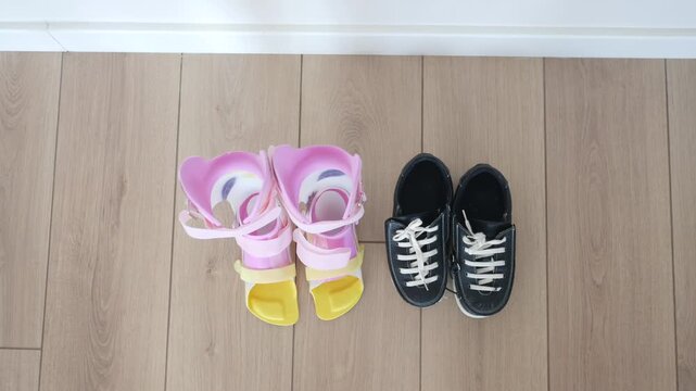 A pair of children's ankle-foot orthoses afo and black athletic shoes resting on a wooden floor in a high-angle shot