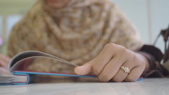 Close up of muslim woman hand wearing diamond ring and flipping pages of menu book in restaurant