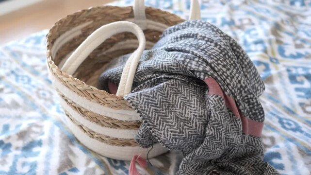 Close up of patterned woven scarf draped inside small decorative basket on blue print bed sheet