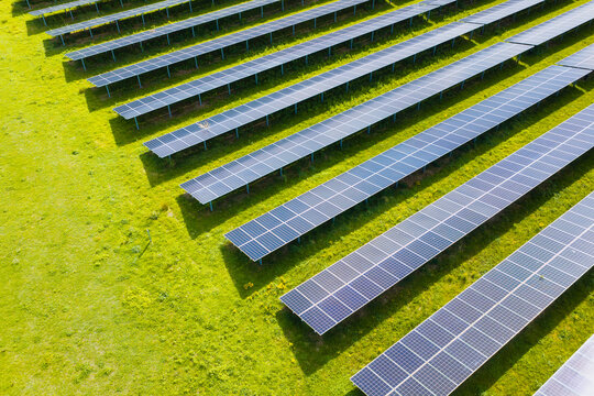 Solar panels installed in a large green field generating clean energy. Aerial view. Autonomous solar power station in a rural landscape.