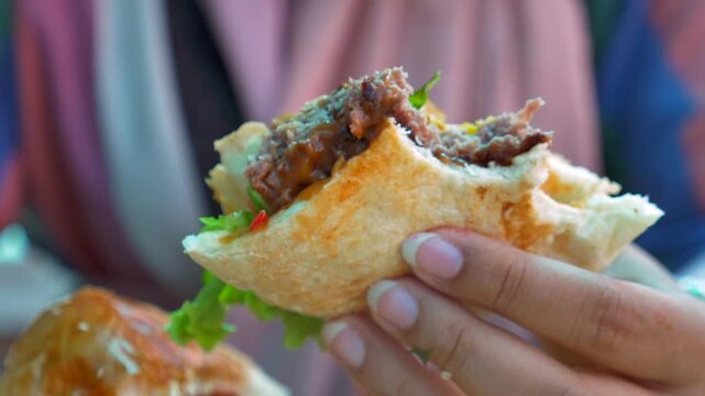 Close up of person holding and eating delicious fresh juicy burger with beef patty lettuce and sauce