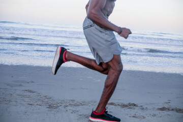 Obraz premium Athletic Black man running along a beach at sunrise, side view