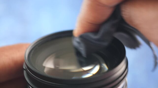 A close up view of person cleaning a dirty camera lens with a microfiber cloth, dust removal process to ensure clear photography, dynamic footage