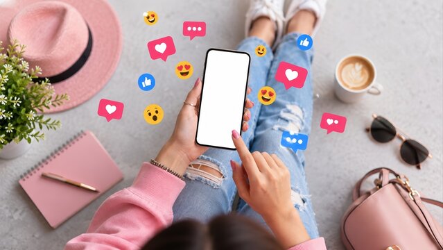 woman holding smartphone with blank white screen surrounded by social media reactions, pink accessories and coffee