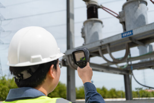 Substation inspection during a patrol shows one technician in a hard hat aiming a thermal camera at the circuit breaker.