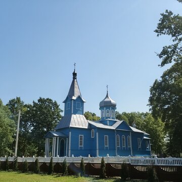 Beautiful blue wooden Orthodox church with silver domes behind a white fence under a clear sky