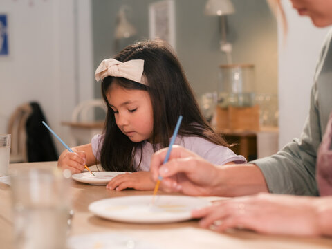 Girl painting plate near her mom at studio