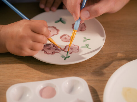 Children and Parent Paint Flowers on a Plate Together at a Table