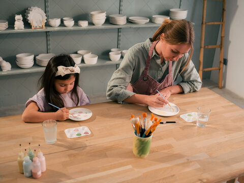 Mother and daughter are focused on painting ceramic plates