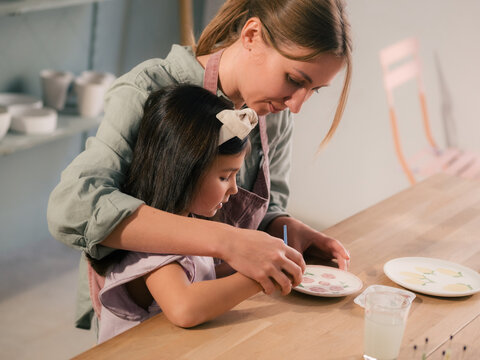 Mother teaching her daughter painting dishes