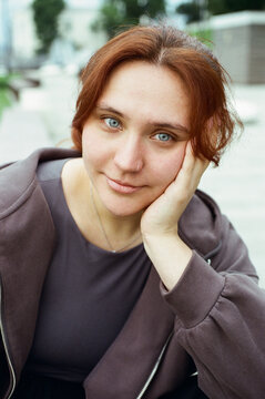 A redheaded woman rests her cheek on her hand outdoors