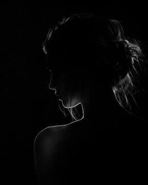 Sensual monochrome woman profile portrait highlighted by dramatic edge rim light in total darkness, moody atmospheric fine art boudoir photography for luxury cosmetics branding