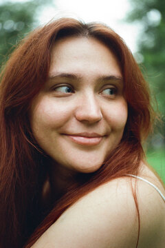 A red-haired woman glances sideways with a quiet smile