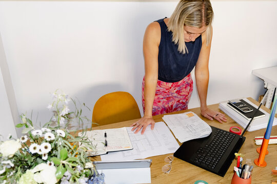 Female architect on phone reviewing plans in home office