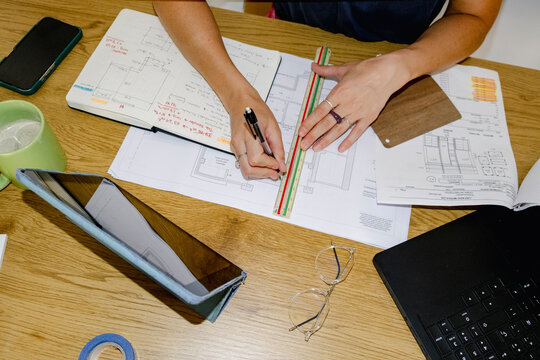 Architect drawing measurements on floor plans at desk