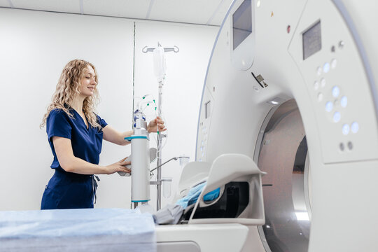 Female radiology technologist preparing contrast injector system beside CT scanner in modern diagnostic center.