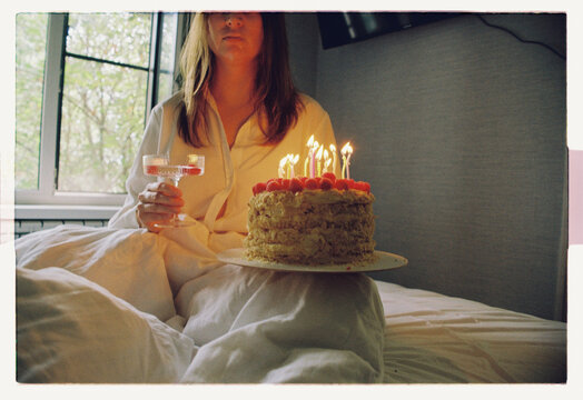 A woman sits in bed with a birthday cake and champagne coupe