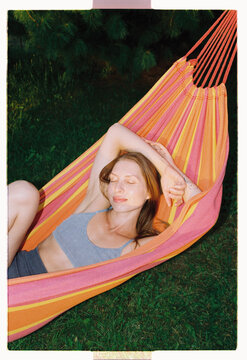 A woman rests with closed eyes in a striped hammock outdoors